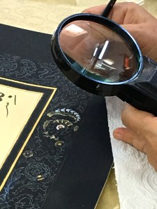 Another teacher shows us how she uses a magnifying glass to paint Tezhip illuminations on manuscripts, scrolls, and books. In this case, she's creating a border for a matt that surrounds a verse of the Quran.